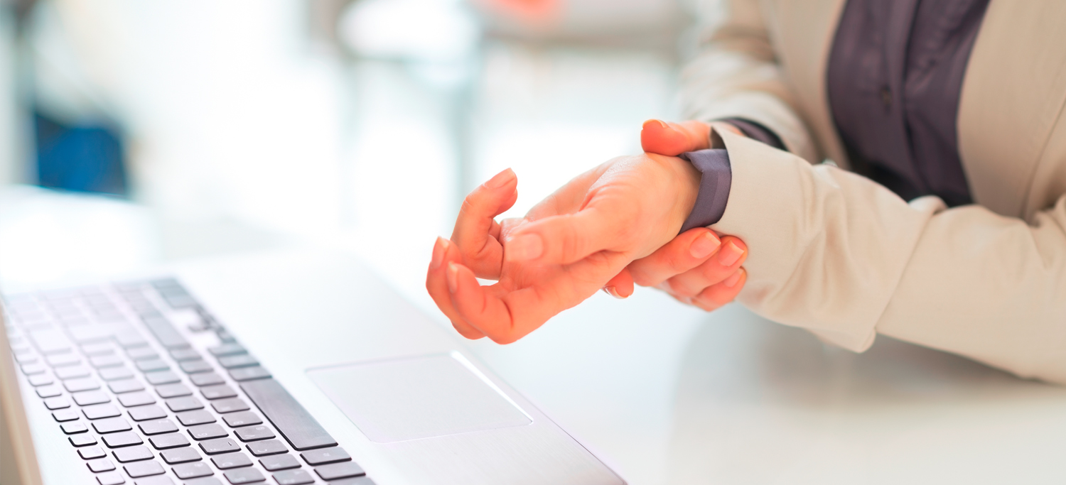 A woman sits at her desk and rubs her wrists.